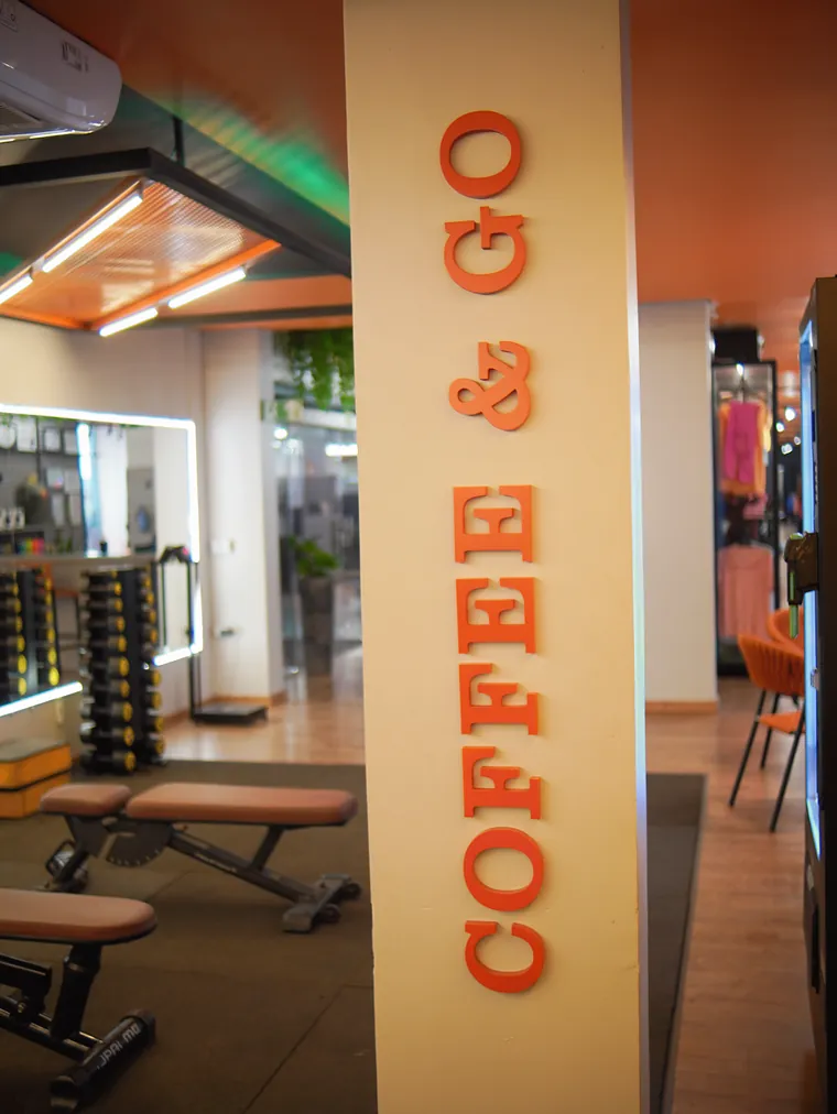 Coluna clara com as letras Coffee & Go em vermelho, na vertical, e bancos de musculação ao lado.
