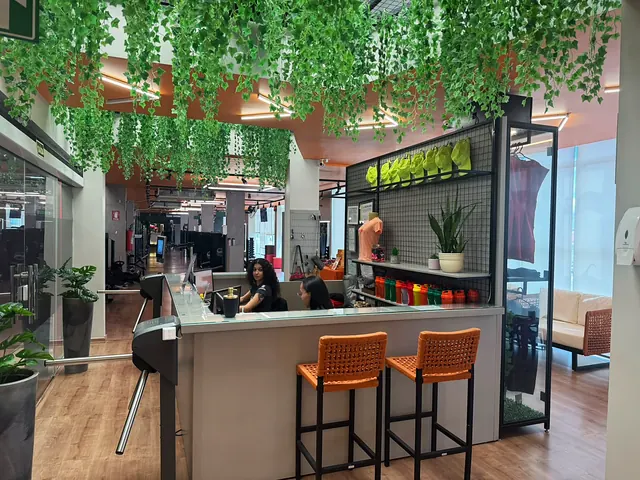 Balcão de convivência da academia, com banquetas, plantas e o salão ao fundo.