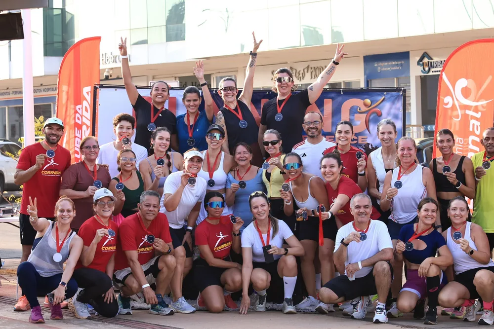 Dezenas de corredores do clube reunidos depois de uma prova de rua, de medalha no pescoço, diante dos banners da organização.
