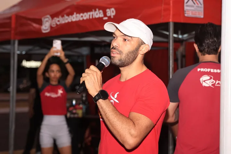 Professor de camisa vermelha do clube falando ao microfone sob a tenda, antes do treino.