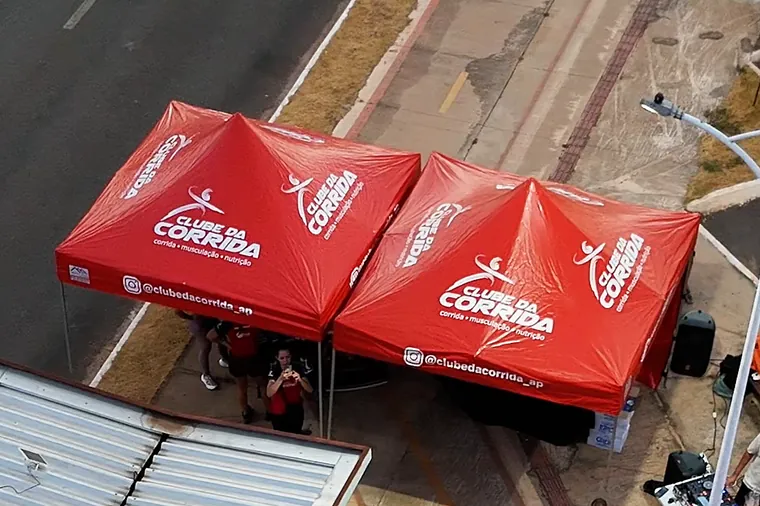 As duas tendas vermelhas do Clube da Corrida vistas de cima, na calçada ao lado da avenida.