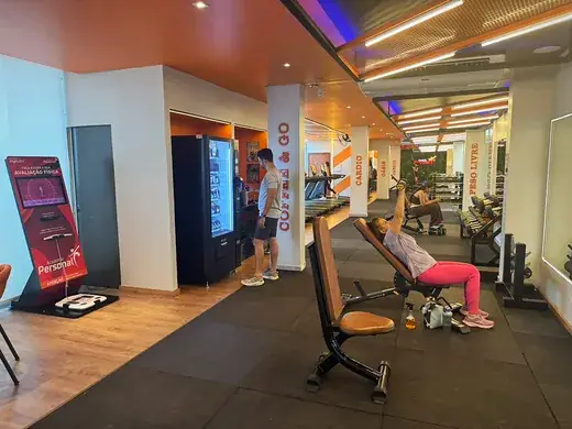 Entrada do salão, com o totem da avaliação física e as máquinas de conveniência encostadas na parede.
