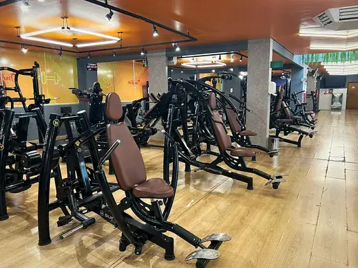 Fileira de estações guiadas de musculação, com bancos estofados e placas de carga.