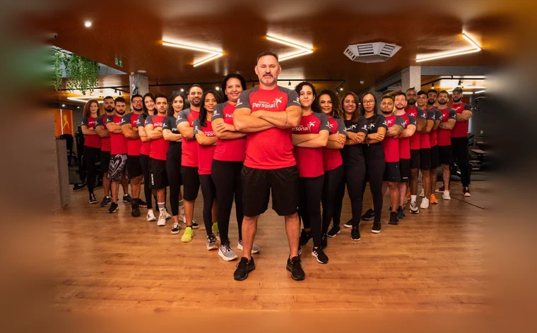 A equipe da Academia Personal reunida no salão: mais de vinte profissionais uniformizados, de braços cruzados, com o professor à frente.