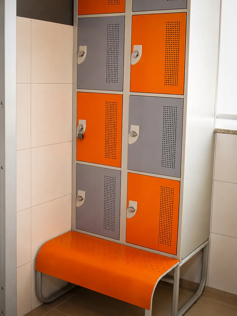 Armários de porta laranja e cinza sobre um banco laranja, no vestiário.
