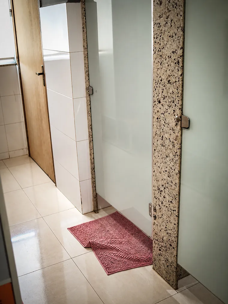 Box de chuveiro com porta de vidro fosco e tapete, no vestiário.